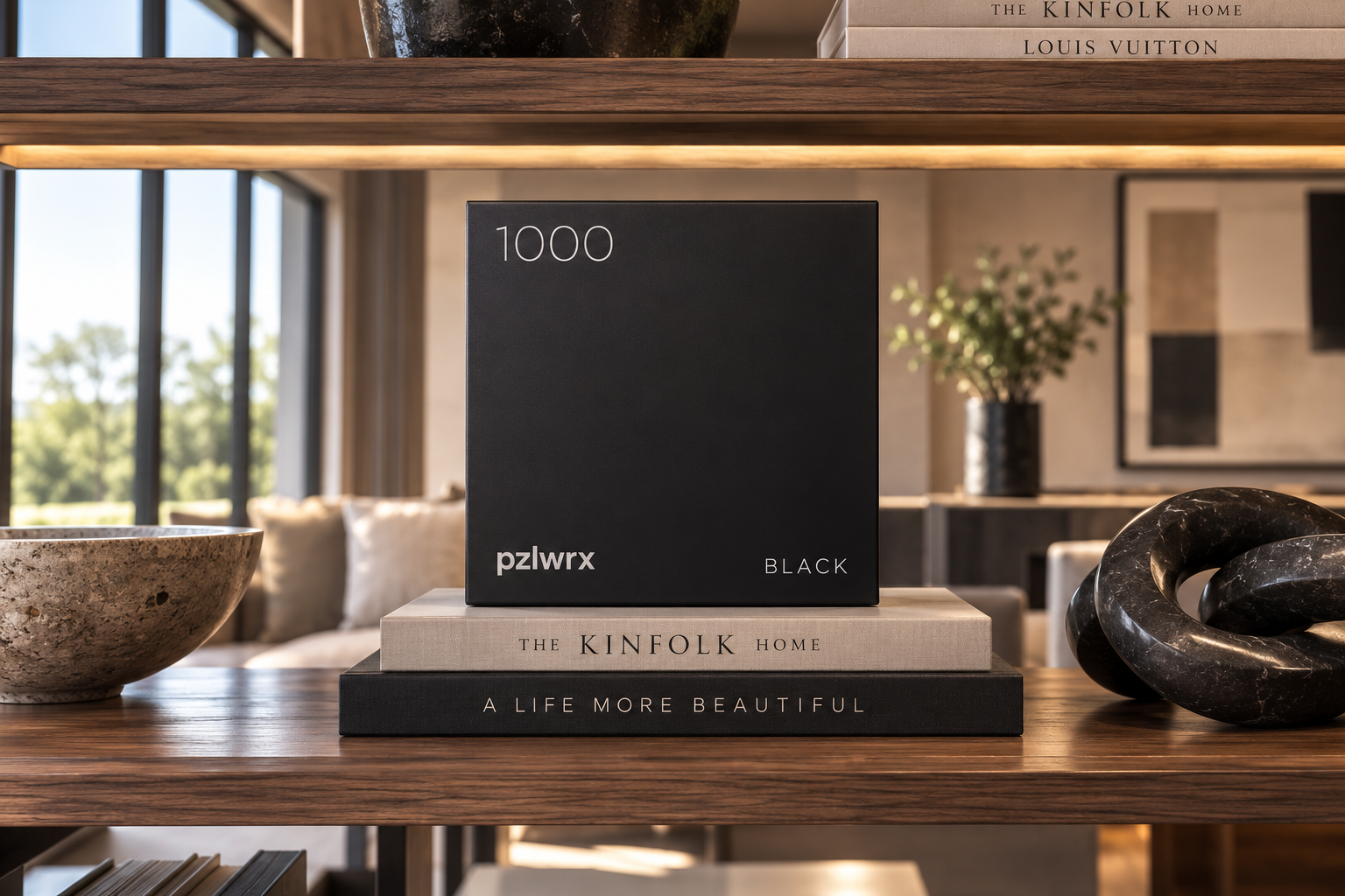 A styled shelf with design books, the pzlwrx 1000 Black puzzle box, a stone bowl and marble sculpture in a modern living room